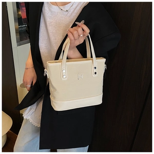 Close-up of beige canvas bucket bag with leather trim and gold metal logo detail