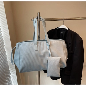 Détail d'un sac cabas tressé bleu clair avec sa pochette sur un présentoir