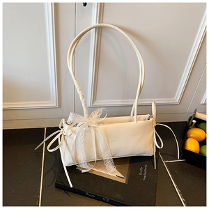 Detail of cream shoulder bag with delicate white lace bows and slim top handles