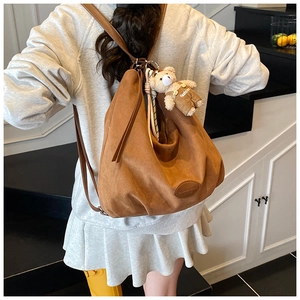Detailed shot of brown suede backpack featuring a cute plush bear pendant and soft texture