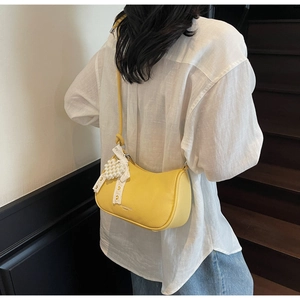 Dettaglio borsa in pelle gialla con fiocco in pizzo bianco e ciondolo cuore perla