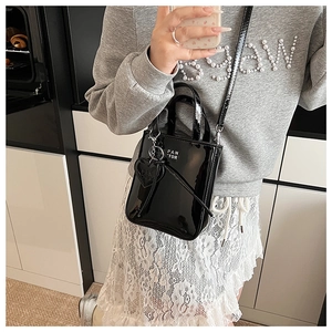 Detail of black patent leather mini bag with heart charm and white text logo branding