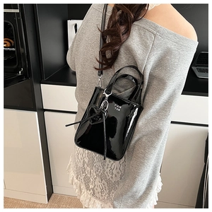 Close-up of black patent leather crossbody bag with heart charm shown on model