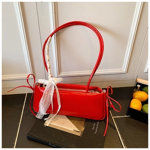 Detail of red patent leather shoulder bag with white lace bow on black book backdrop