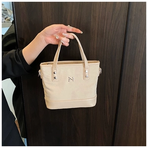 Detail of cream bucket bag showing leather handles and metal logo on canvas material