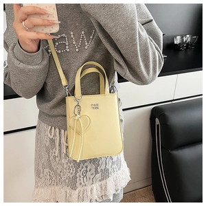 Detail of yellow patent leather mini bag with heart charm and silver logo on a model
