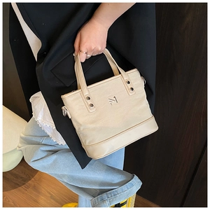 Detail view of stylish beige canvas bucket bag with leather trim and metal logo