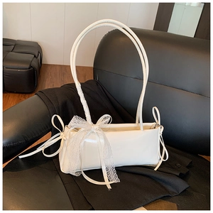 Close-up of white leather shoulder bag featuring delicate lace bow and long ribbons