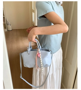 Detail of light blue leather bucket bag featuring a unique knotted handle and decorative charm