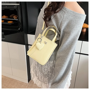Detail of cream yellow mini crossbody bag with silver PAN TOR logo and heart pendant