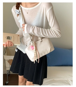 Minimalist beige bucket bag with pink heart pendant and woven tassel detail on top