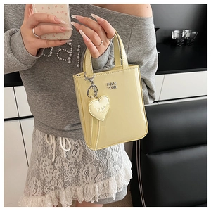 Close-up of a pale yellow patent leather handbag with silver logo and heart pendant