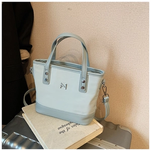 Detail of light blue bucket bag with metal M logo and adjustable strap on a book