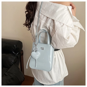 Detailed view of light blue patent leather mini tote bag with heart charm and logo