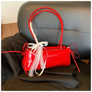 Detail of red glossy shoulder bag featuring large white lace bow and drawstring side