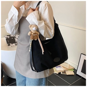 Detail of black canvas hobo bag with leather logo patch and cute teddy bear charm
