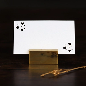 Close-up of golden rectangular metal place card holder with heart motif card on wood
