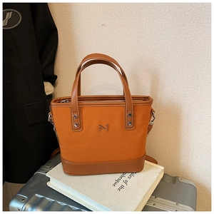 Close-up of the orange-brown tote bag featuring silver M-logo and leather拼接 details