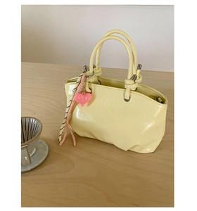 Detail of light yellow patent leather bucket bag with pink heart charm and striped ribbon