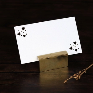 Golden metal place card holder with elegant heart-shaped cutout card for weddings