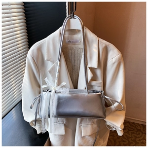 Detail of silver metallic underarm bag featuring delicate white lace ribbon and side bows