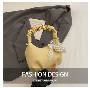 Detail of light yellow crescent bag with pleated handle and pearl lace bow charms