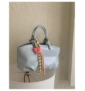 Detail of light blue pleated bucket bag featuring a knotted handle and heart charm