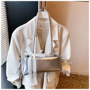 Detail of silver metallic handbag featuring delicate white lace bow and twin slim straps