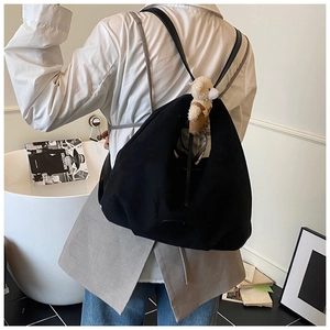 Detail of minimalist black tote backpack with a cute teddy bear charm on model's back