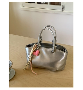 Close-up of silver textured bucket bag with pink heart charm and woven strap detail