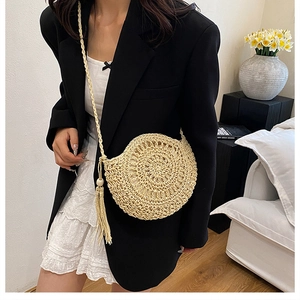Dettaglio borsa tonda in paglia intrecciata con motivo a spirale e nappe decorative