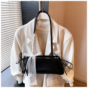 Detailed shot of a black patent leather underarm bag with white lace bow and drawstring design