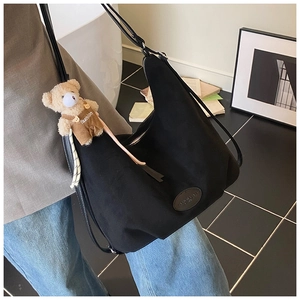 Detail of black crescent hobo tote with a cute bear pendant and textured side leather patch