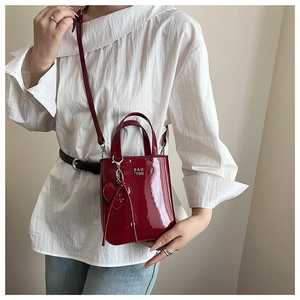 Detail view of red glossy patent leather handbag with silver logo and heart charm