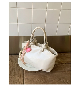 Detail of cream leather bucket bag with pink heart charm and knot handle on a plate