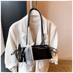 Detail of glossy black shoulder bag with a large white lace bow and long strap
