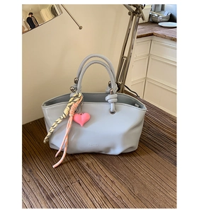 Close-up of light blue leather bucket bag with pink heart charm and braided rope detail