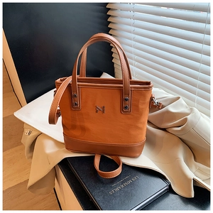 Detailed close-up of brown canvas and leather bucket bag with metallic logo and strap