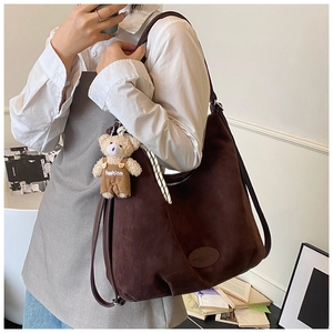 Close-up of brown suede tote bag featuring a cute bear charm and oval brand logo