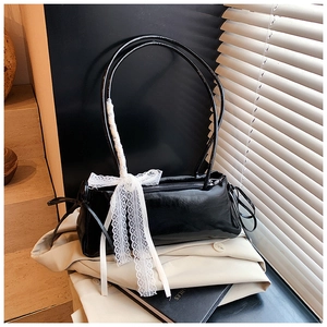 Detail of black glossy shoulder bag featuring a white lace ribbon on the handle