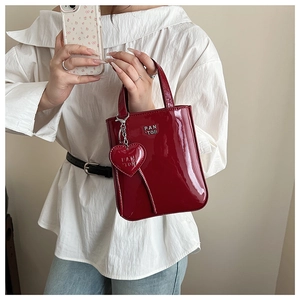 Detail of dark red patent leather handbag with metal brand logo and heart charm