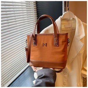 Detail of a brown canvas and leather bucket bag with top handles and a metal logo