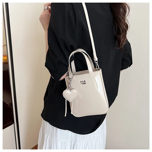Detail of cream patent leather crossbody bag featuring heart charm and PAN TOR logo
