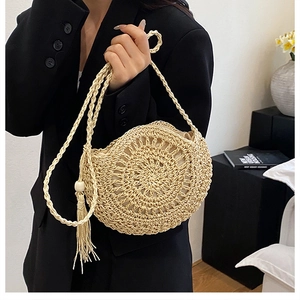 Dettaglio di borsa rotonda in paglia intrecciata a mano con frange boho e perle di legno