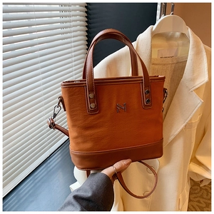 Detail of canvas bucket bag with brown leather trim and metallic logo accent