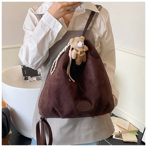 Close-up of brown suede hobo tote with wide strap, contrast rope, and plush bear charm