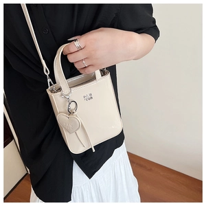 Detail of light beige patent leather handbag featuring heart charm and PAN TOR logo