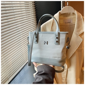 Detail of light blue leather bucket bag with metal logo and adjustable shoulder strap