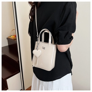 Detail of cream patent leather handbag featuring silver heart charm and metal logo