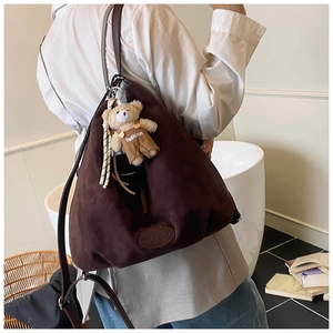 Detail of a large dark brown suede tote bag with a cute bear charm on a model side